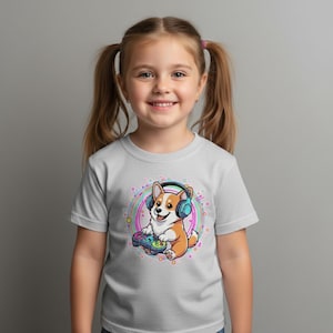 Może przedstawiać: Jasnoszara koszulka z kreskówkowym corgi w słuchawkach i trzymającym kontroler do gier. Corgi otoczony jest kolorowym, okrągłym wzorem. Koszulkę nosi mała dziewczynka z warkoczykami.