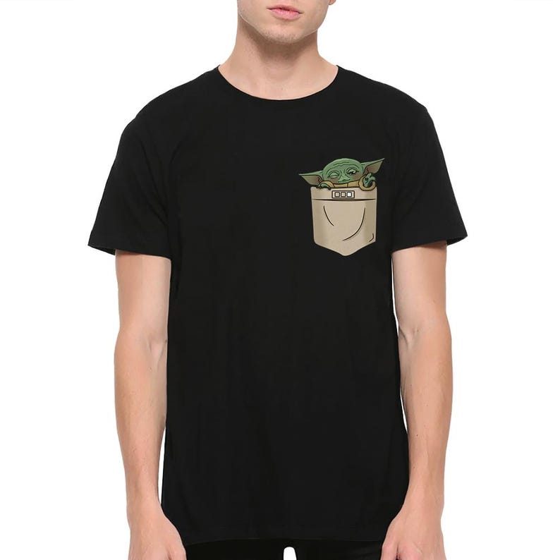 May include: Black t-shirt featuring a pocket with a graphic of Grogu, also known as Baby Yoda, peeking out. The pocket is tan, and Grogu is green with large eyes. The t-shirt is a short-sleeved crew neck.