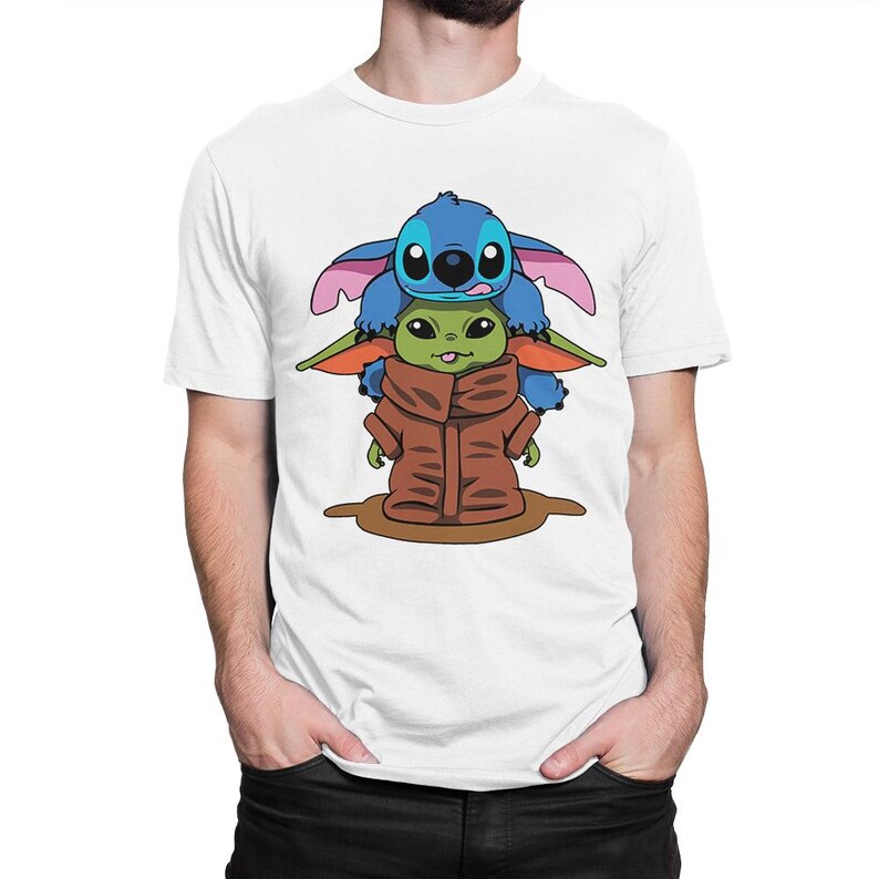 May include: White t-shirt with a cartoon graphic of Stitch from Lilo & Stitch and Grogu (Baby Yoda) from The Mandalorian. Stitch is blue with large ears, and Grogu is green and wearing a brown cloak. The characters are stacked on top of each other.