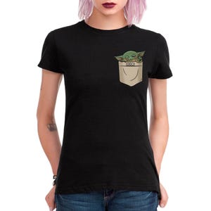 May include: Black t-shirt featuring a pocket design with a green and tan illustration of a character from a popular science fiction series. The pocket design is on the left chest area of the shirt.