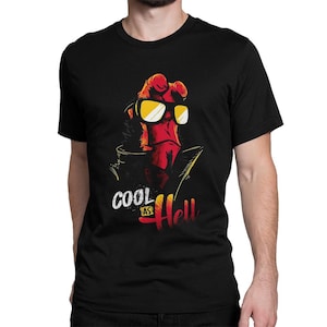 May include: Black t-shirt featuring a red character with yellow-tinted sunglasses. The graphic includes the text "COOL as Hell" in white and red. The shirt is a crew neck style.