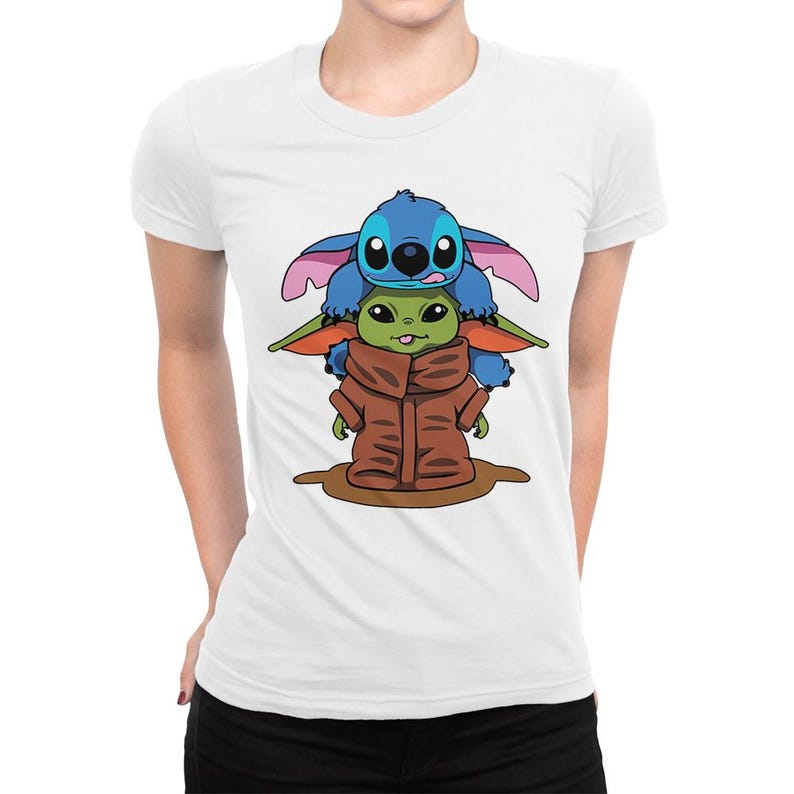 May include: White t-shirt with a graphic of Stitch and Grogu. Stitch, in blue, is on top of Grogu, who is wearing a brown cloak. The design is centrally placed on the shirt.