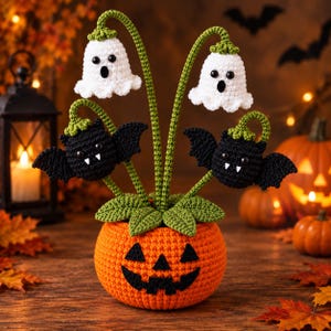 Può includere: Una decorazione di Halloween all'uncinetto con una base a forma di zucca arancione e un volto di jack-o'-lantern nero. Due figure di fantasmi bianchi e due di pipistrelli neri con zanne bianche sono fissate su steli verdi.