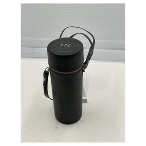 May include: A black cylindrical case with a zipper closure and a handle. The top of the case has the word "PRO" embossed on it. The case has a textured surface and a strap for carrying.