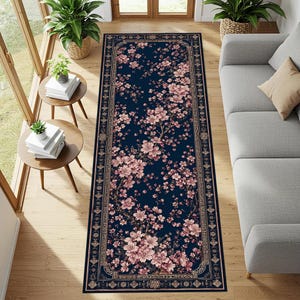Peut inclure: Un tapis rectangulaire bleu marine avec un motif floral. Le tapis présente des fleurs roses et une bordure décorative dans des tons or et marron. Le tapis est posé sur un sol en bois.