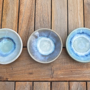Może przedstawiać: Trzy małe, okrągłe miseczki ceramiczne z wykończeniem z reaktywnego szkliwa. Każda miseczka ma unikalny gradient kolorów, przechodzący od jasnego środka do głębokiego niebieskiego pierścienia i jasnej zewnętrznej krawędzi, tworząc wyraźny wzór.