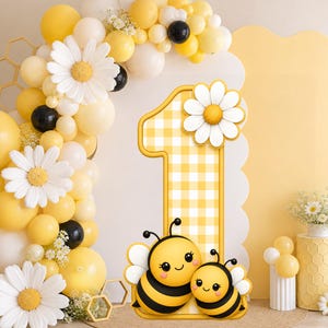 Peut inclure: Décoration de fête du premier anniversaire sur le thème jaune et blanc. Le chiffre un est décoré d'un motif vichy jaune et d'une marguerite blanche. Deux abeilles de dessin animé sont devant le chiffre. Une arche de ballons et d'autres décorations complètent la scène.