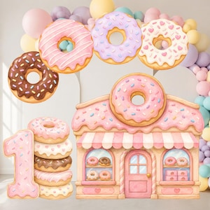 May include: A decorative set featuring a large number one shaped like a pink frosted donut, a donut shop building with a pink donut roof, and several individual floating donuts in chocolate, pink, and white frosting with colorful sprinkles.