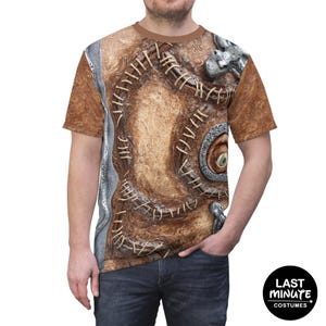 May include: Brown t-shirt featuring a detailed, textured design of a spellbook cover. The design includes stitched edges, a large eye, and metal clasps. The shirt is a costume item, perfect for Halloween or themed events.