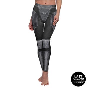 May include: Black leggings with a printed design resembling armor plating. The leggings feature a high waist and a detailed, textured appearance, with metallic gray accents. The design includes knee and thigh armor elements, creating a realistic look.