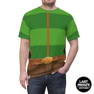 May include: Green t-shirt with a costume design. The shirt features a green top with a vertical orange zipper, brown belt with a gold buckle, and brown pants design. The shirt is a costume from Last Minute Costumes.