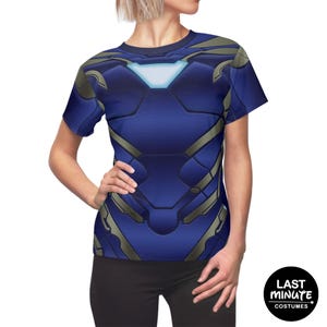 May include: A blue t-shirt featuring a detailed design resembling armor, with accents in gray and a glowing white chest emblem. The shirt is short-sleeved and has a crew neck. The image includes the text "LAST MINUTE COSTUMES" in a circular logo.