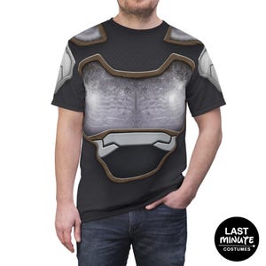 May include: Black t-shirt with a printed design resembling armor. The design includes silver and brown accents, creating a realistic armored appearance. The shirt has a crew neck and short sleeves. The Last Minute Costumes logo is visible.