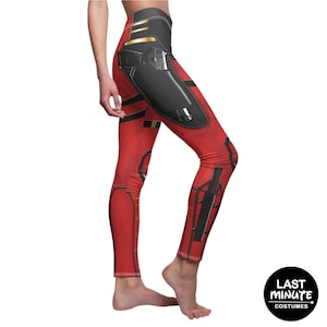 May include: Red leggings with black and gold accents, featuring a detailed design. The leggings have a high waistband and a form-fitting silhouette. The design includes panels and details that resemble armor. The Last Minute Costumes logo is visible.