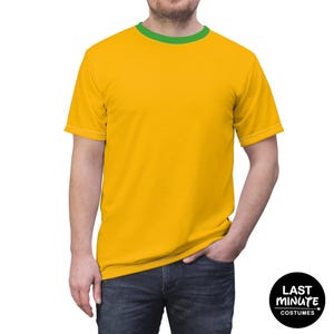 Puede incluir: Una camiseta amarilla con cuello verde y ribete blanco. La camiseta de manga corta tiene un diseño sencillo. La camiseta forma parte de la colección "Last Minute Costumes".