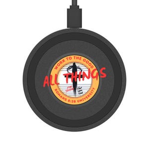 Peut inclure: Un chargeur sans fil noir de forme circulaire. Le centre présente une croix avec les mots "ALL THINGS" en rouge et "WORK TO THE GOOD" en cercle. Le texte supplémentaire comprend "ROMANS 8:28 UNIVERSITY".