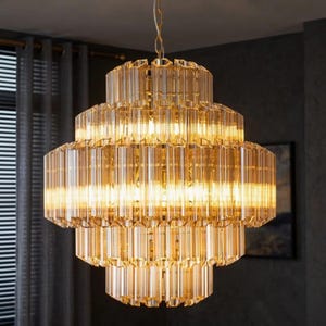 May include: A tiered chandelier with a warm amber glow. The fixture is composed of multiple layers of rectangular crystal prisms, suspended from a gold chain. The light fixture is a decorative element for interior spaces.