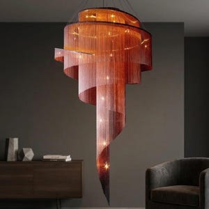 Puede incluir: Una lámpara de araña moderna en espiral con un diseño en cascada. La lámpara presenta capas de hebras de color cobre que crean un efecto degradado, pasando de claro a oscuro. Pequeñas luces están intercaladas.