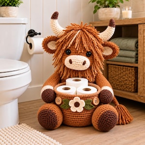 May include: A crocheted highland cow figurine with shaggy brown yarn, cream-colored horns, and black eyes. The cow holds a round, brown crocheted basket containing three rolls of white toilet paper, decorated with a white flower and two buttons.