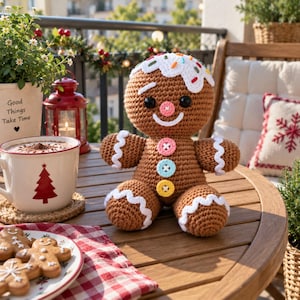 May include: A brown crocheted gingerbread person doll with white icing details, a pink nose, and three colorful buttons on its chest. The doll features black eyes and a white smile, sitting on a wooden table next to a mug and gingerbread cookies.