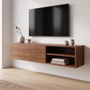 May include: A wooden floating media unit with a closed cabinet and open shelving, mounted below a large black television. The unit has a natural wood grain finish. Decorative vases and books are on the unit.