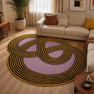 May include: A round area rug with a unique design. The rug features a light purple center with a pattern of black and gold curved lines. The rug is placed on a hardwood floor in a living room setting.