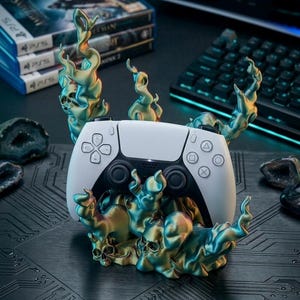 以下が含まれることがあります： 白と黒のPlayStation 5コントローラーが装飾的なスタンドに置かれています。スタンドは、頭蓋骨と炎のデザインで、ティールとゴールドのアクセントが付いています。ビデオゲームケースとキーボードが背景にあります。