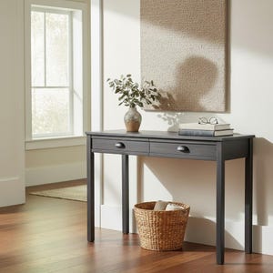 Puede incluir: Una consola de madera gris oscuro con dos cajones, una cesta de mimbre y un jarrón con vegetación. La mesa tiene una parte superior rectangular y cuatro patas rectas. Una alfombra cuelga de la pared detrás de la mesa. La mesa está en una habitación bien iluminada.