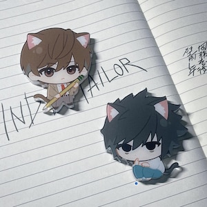 May include: Two anime-style character stickers with cat ears on a lined notebook. One character has brown hair and a pencil, the other has black hair and is sitting. The word "TAILOR" is written on the page.
