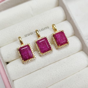 May include: Three rectangular pendants featuring deep pink gemstones set in gold-toned metal frames, each surrounded by a border of small clear stones. Each pendant has a gold-toned bail at the top. The text JEWELSYLALITA is visible in the background.