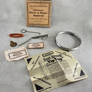 May include: A vintage sewing machine repair kit with various metal and rubber parts, including a silver ring, springs, and a small key. The kit includes a box and paper instructions with German text.