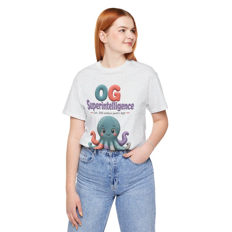 May include: A light gray short-sleeve t-shirt featuring a graphic of a teal octopus with pink cheeks. Above the octopus, the text reads "OG Superintelligence" in large, colorful letters, followed by the smaller text "Est. 300 million years ago."