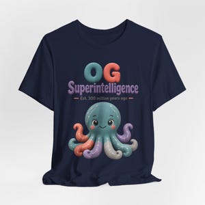 May include: A navy blue short-sleeve t-shirt featuring a graphic of a teal octopus with constellation patterns on its tentacles. Above the octopus, the text reads "OG Superintelligence" and "Est. 300 million years ago" in colorful, rounded lettering.
