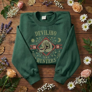 May include: A dark green crewneck sweatshirt featuring a central graphic with the text DEVILJHO HUNTERS, a stylized monster illustration, the numbers 20 and 10, and various geometric symbols arranged in a diamond pattern on the front chest.