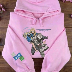 May include: A light pink hooded sweatshirt featuring an embroidered graphic of a blonde character in a blue jacket riding on the back of a futuristic armored figure. The text "Visualization complete. Initiating hack!" is printed above the graphic.