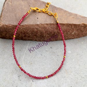 Puede incluir: Una pulsera delicada con pequeñas cuentas facetadas de color rosa intenso intercaladas con diminutas esferas de metal dorado. La pieza incluye una cadena extensora de metal dorado con cierre de mosquetón. El texto Khatugems es visible en morado.