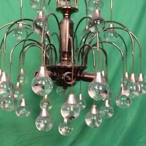 May include: A vintage chandelier with a brass frame and multiple clear glass globe lights. The chandelier has a central fixture with curved arms extending outwards, each holding a glass globe. The background is a solid green.
