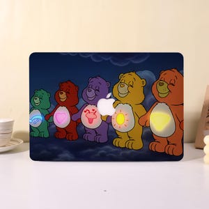May include: A laptop skin featuring five colorful cartoon bears standing against a dark blue cloudy sky. The bears are green, red, purple, yellow, and orange, each with a glowing symbol on their belly. An Apple logo is visible in the center.