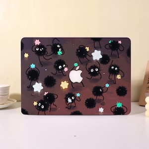 May include: A laptop case featuring a repeating pattern of black, fluffy creatures with large eyes and star-shaped accents in various colors. The Apple logo is visible in the center of the case.