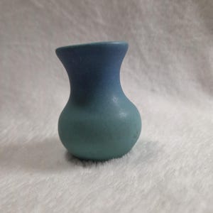 May include: A small, two-toned ceramic vase. The top is a deep blue, transitioning to a teal green at the base. The vase has a rounded body and a flared opening, suitable for small floral arrangements or decorative display.