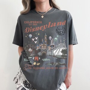 May include: Dark gray t-shirt with a Disneyland graphic. The design includes the Disneyland logo, a castle, Mickey Mouse, a Ferris wheel, and the text "The happiest place on earth."