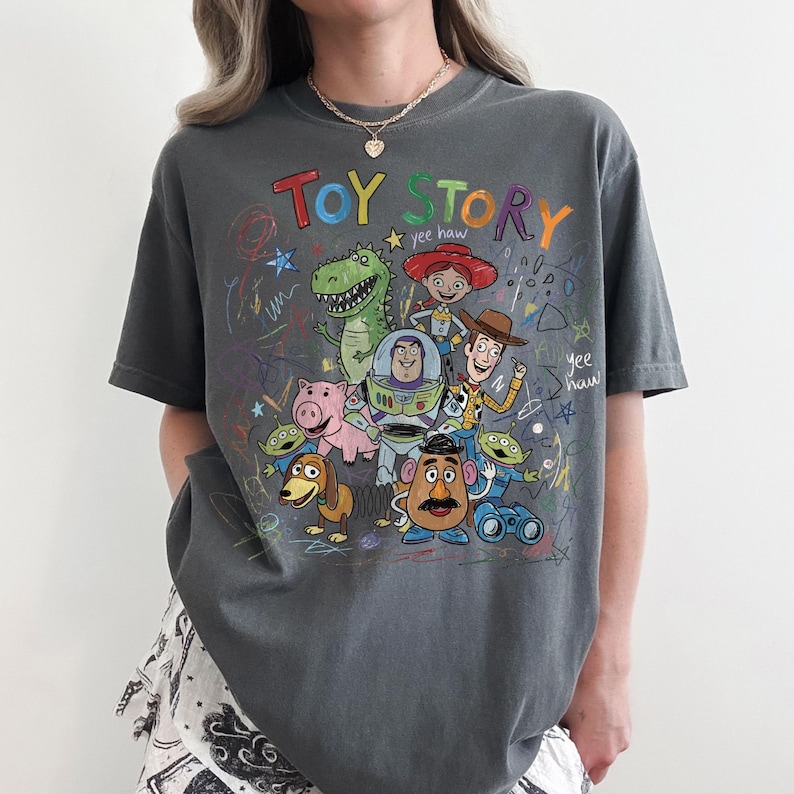 Peut inclure: T-shirt gris fonc&eacute; avec un graphisme color&eacute; des personnages du film d'animation "Toy Story". Le motif comprend les mots "Toy Story" dans une police ludique, ainsi que des dessins de Woody, Buzz l'&Eacute;clair et d'autres personnages.