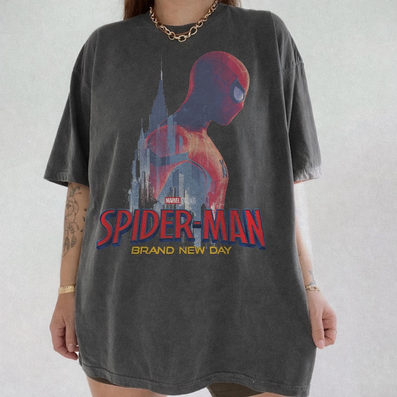 Op de afbeelding: Een antracietgrijs T-shirt met korte mouwen en een afbeelding van Spider-Man in profiel tegen een stadssilhouet. De tekst Marvel Studios Spider-Man Brand New Day staat in rode en gele letters op het borstgedeelte van het kledingstuk.