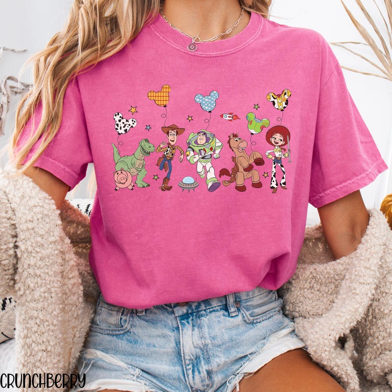 Puede incluir: Una camiseta de manga corta de color rosa brillante con un estampado gr&aacute;fico de los personajes de Toy Story, incluyendo a Woody, Buzz Lightyear, Jessie, Rex, Bullseye y Hamm. El dise&ntilde;o incluye globos con forma de Mickey Mouse y estrellas.