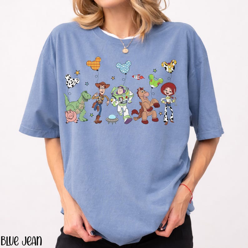 Puede incluir: Una camiseta azul de manga corta con un estampado gr&aacute;fico de personajes de Toy Story, incluyendo a Woody, Buzz Lightyear, Jessie, Rex, Perdig&oacute;n y Hamm. Los personajes sostienen globos coloridos con forma de orejas de Mickey Mouse.