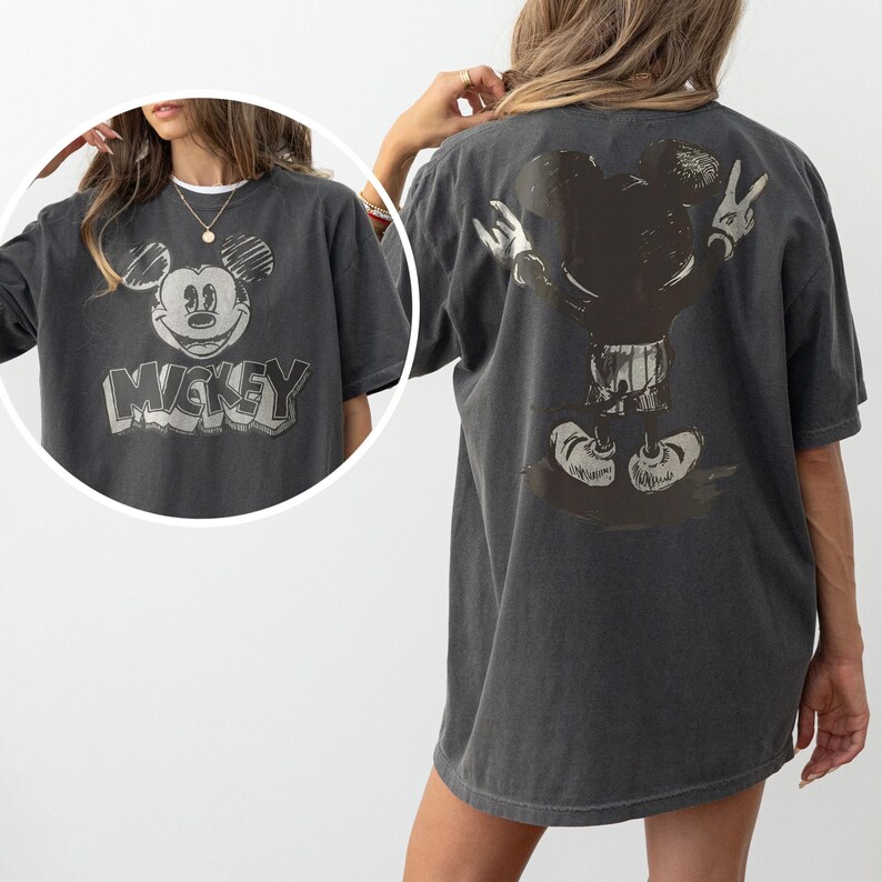 May include: A charcoal gray short-sleeve t-shirt featuring a distressed graphic of Mickey Mouse on the front and back. The front displays a sketch-style Mickey face with the text Mickey below it, while the back shows a full-body rear view of Mickey.