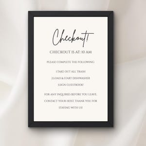 Puede incluir: Un letrero enmarcado con la palabra "Checkout!" en escritura elegante. El letrero proporciona instrucciones para los huéspedes, incluido el horario de salida y tareas como sacar la basura y poner en marcha el lavavajillas. El fondo es de color blanco roto.