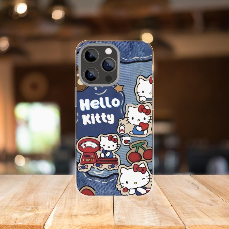 Puede incluir: Una funda de tel&eacute;fono con un dise&ntilde;o similar al denim y gr&aacute;ficos de Hello Kitty. La funda incluye el texto "Hello Kitty" y varias ilustraciones del personaje, junto con cerezas y una balanza.
