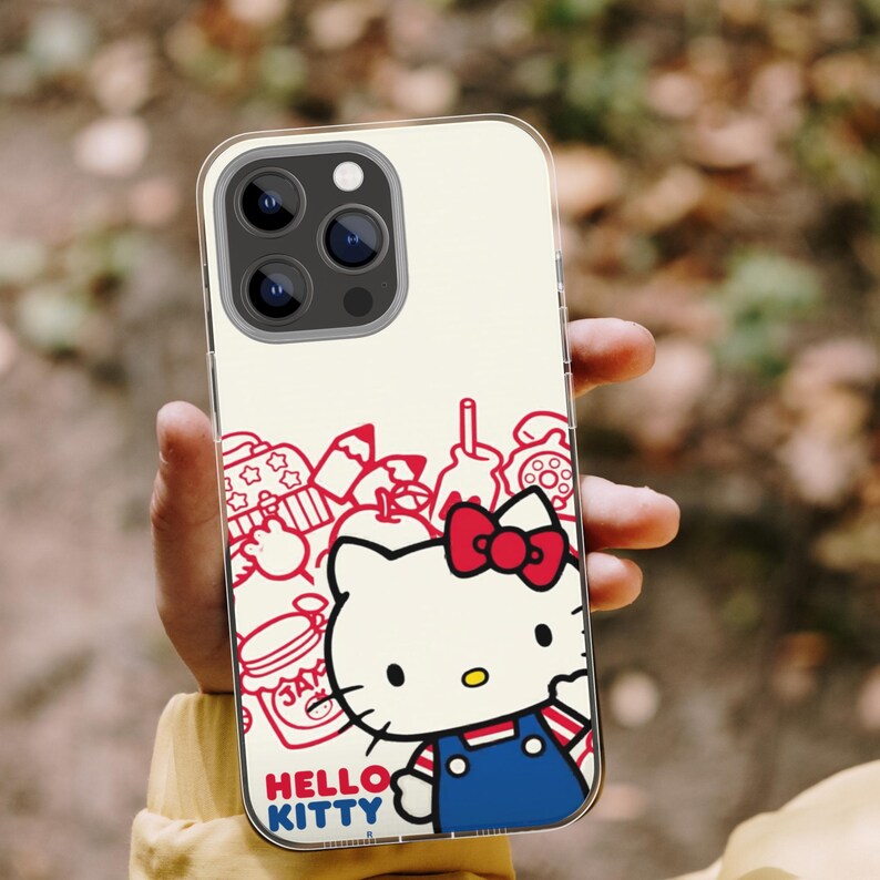 Puede incluir: Funda transparente para tel&eacute;fono con dise&ntilde;o de Hello Kitty. La funda tiene un fondo crema con dibujos lineales rojos y un personaje de Hello Kitty con un atuendo azul y un lazo rojo. Las palabras "HELLO KITTY" est&aacute;n en la parte inferior.