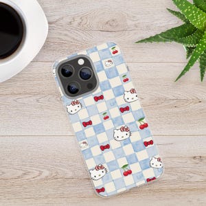 Puede incluir: Una funda transparente para tel&eacute;fono con un dise&ntilde;o de cuadros azules y blancos, decorada con Hello Kitty, lazos rojos y cerezas. La funda est&aacute; dise&ntilde;ada para un smartphone y tiene un recorte para la c&aacute;mara.